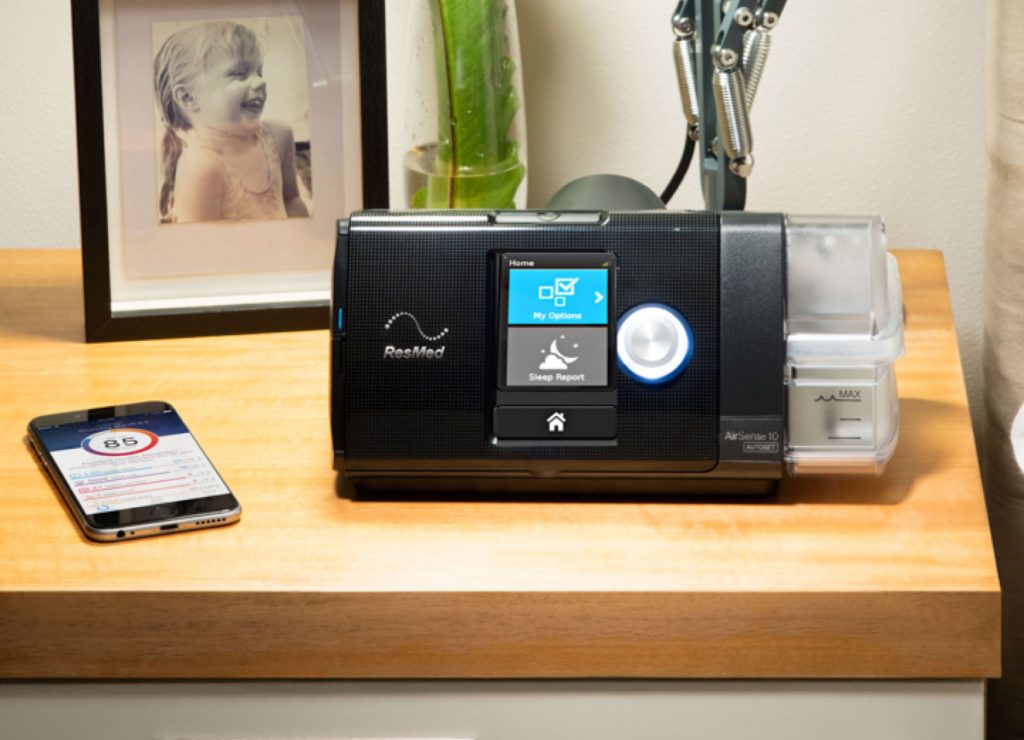 ResMed AirSense 10 CPAP machine beside a phone showing the myAir therapy app